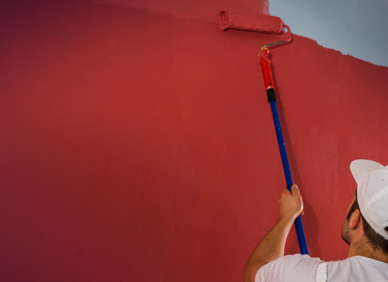Een man met een pet verft een blauwe muur rood met een verfroller